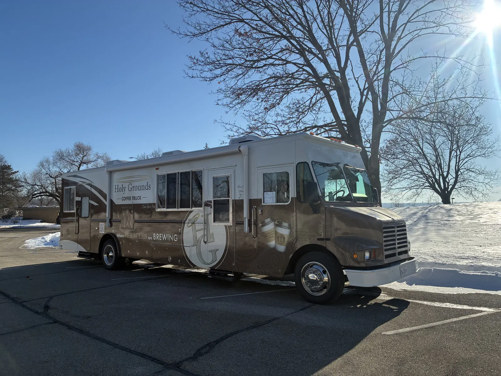Holy Grounds Coffee Truck parked beside snow on a sunny winter day